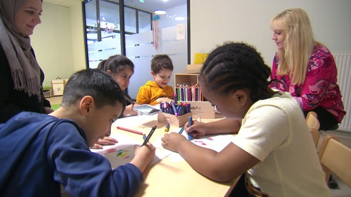 Erzieher gucken zu, während die Kinder am Tisch zusammen malen. 