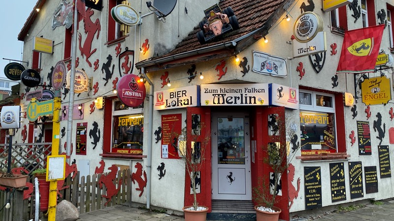 Blick auf ein weißes Gebäude, an dessen Fassade viele Ferrari-Symbole hängen.