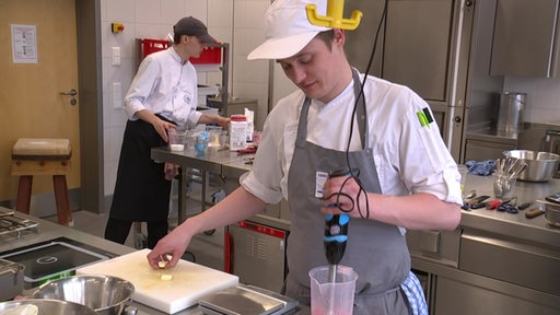 Zwei junge Köche stehen in einer Küche und kochen.