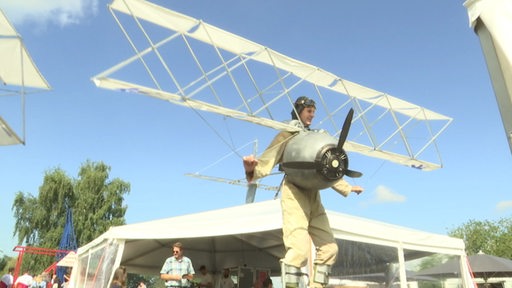 Es ist ein Junge zu sehen, welcher in einem Kostüm steckt, das aussieht wie ein Propellerflugzeug.