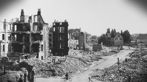 Ein schwarz-weiß Bild von einer Stadt nach Bombenangriffen, es liegen viele Trümmer herum und nur wenige Gebäudereste stehen noch.