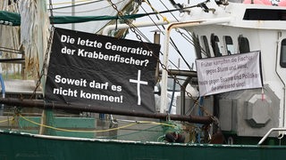 An einem Kutter hängt ein Plakat mit der Aufschrift "Die letzte Generation der Krabbenfischer?" Soweit darf es nicht kommen!".