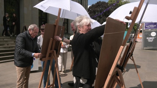 Zu sehen sind mehrere Personen, die vor der Kunsthalle Bilder malen.