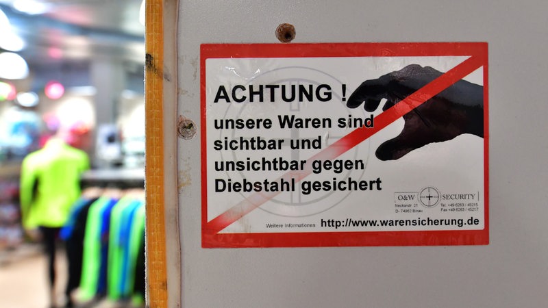 Ein Aufkleber mit der Aufschrift "Achtung ! unsere Waren sind sichtbar und unsichtbar gegen Diebstahl gesichert" ist an der Umkleidekabine in einem Sportgeschäft zu sehen. 