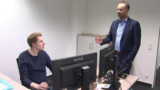 Nils Ruttmann, der neue Vizepräsident des Landessportbundes Bremen, steht in seinem Büro und spricht mit einem Mitarbeiter, der am Schreibtisch sitzt.