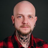 Ein Mann mit Totenkopf-Tattoo am Hals schaut in die Kamera.