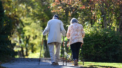 Altes Ehepaar-Rentner -Mann und Frau gehen mit Nordic Walking Stoecken spazieren.