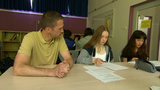 Ein Quereinsteiger-Lehrer unterrichtet zwei Schülerinnen im Klassenraum.