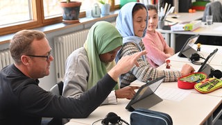 Ein Lehrer zeigt einer Schülerin etwas an einem Tablet.