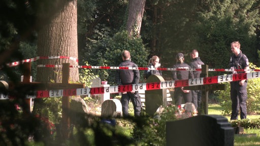 Polizisten stehen auf einem Friedhof nach einem Leichenfund. 