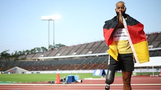 Der Para-Leichtathlet Leon Schäfer steht mit geschlossenen Augen und vor dem Mund zusammengelegten Händen auf einer Tartanbahn, nachdem er Gold im 100 Meter Lauf gewonnen hat.