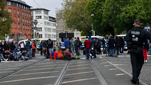 Eine Gruppe von Demonstrierenden auf einer Kreuzung, im Vordergrund ein Polizist.