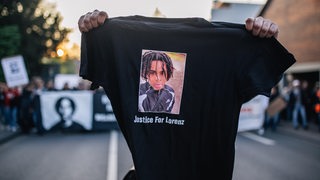 Ein Demonstrant hält vor einer Kundgebung ein schwarzes T-Shirt in die Kamera, auf dem der von Polizeischüssen getötete Lorenz aus Oldenburg abgebildet ist.