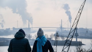 Passanten betrachten bei kühlem Wetter die Köhlbrandbrücke und die umliegenden Industrieanlagen im Hamburger Hafen.