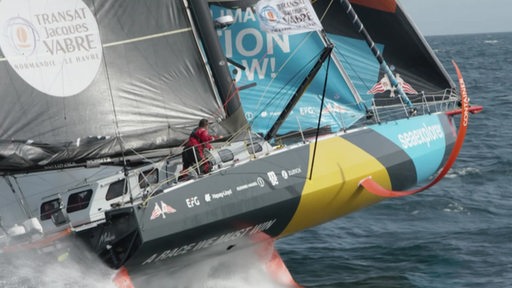 Ein Segelboot fährt auf Foils über dem Wasser, an Deck steht eine Person