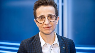 Eine Person (Masha Gessen) mit Brille und kurzen Haaren vor einem blauen Hintergrund.