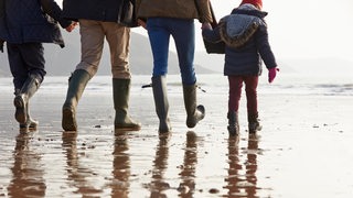 Eine Familie mit 2 Kindern macht in Gummistiefeln eine Wattwanderung.