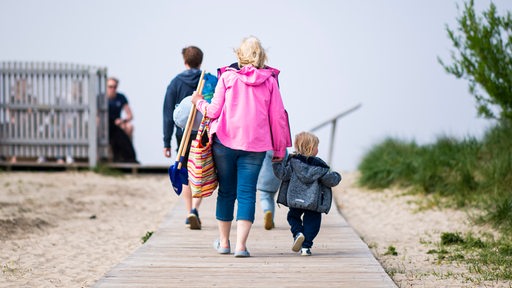 Touristen gehen im Urlaubsort Schillig an den Strand. 