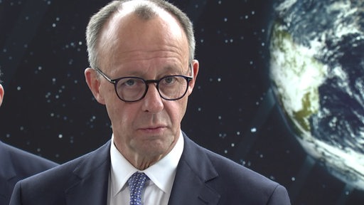 Friedrich Merz und im Hintergrund ein Bild vom Weltall.