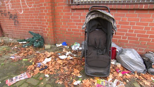 Neben einem alten Kinderwagen liegt eine Menge Müll auf dem Boden