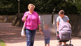 Eine junge Frau mit blonden Haaren geht einen Weg entlang und hält ein Kind an der Hand