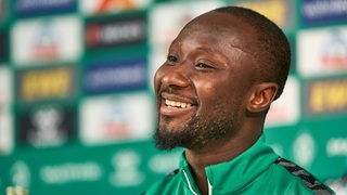 Naby Keita lächelt bei einer Pressekonferenz.