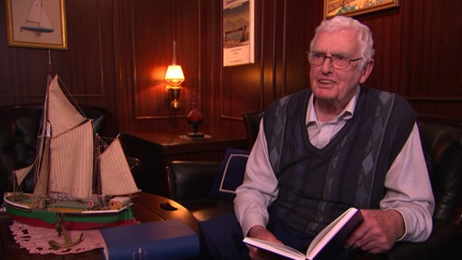 Der Nautiker Harald Ricklefs mit einem Buch in der Hand.