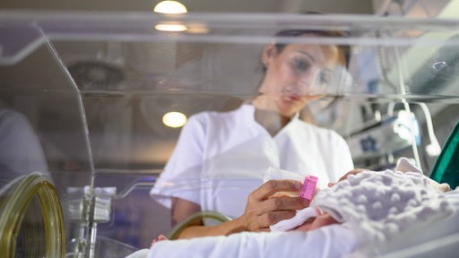 Eine Krankenschwester füttert ein Baby im Brutkasten mit einem Fläschchen.