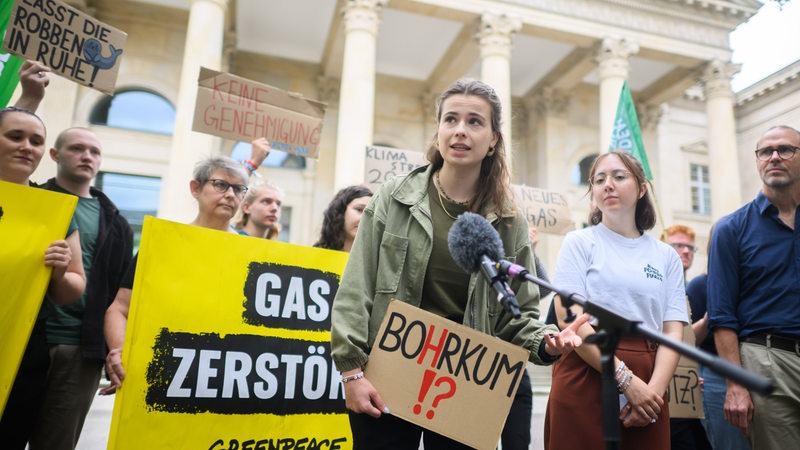 Luisa Neubauer mit einem Schild "Bohrkum", im Hintergrund Demonstranten und der niedersächsische Landtag