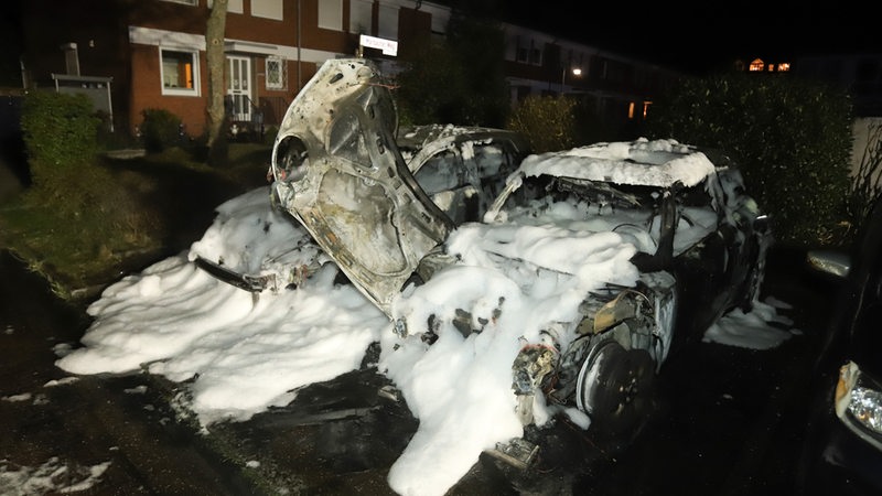 Zwei ausgebrannte Autos stehen nebeneinander. Die Fahrzeuge sind voll mit Löschschaum.