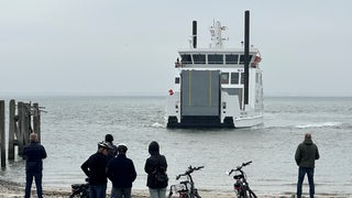 Passanten beobachten in Norderney, wie ein Schiff anlegt. 