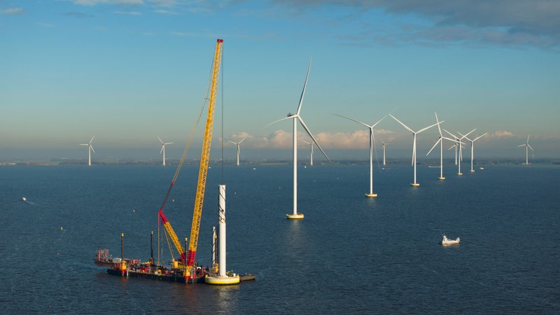 Ein Kran baut eine Offshore-Windkraftanlage zusammen.