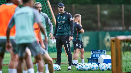 Werder-Trainer Ole Werner steht zwischen seinen Spielern auf dem Trainingsplatz