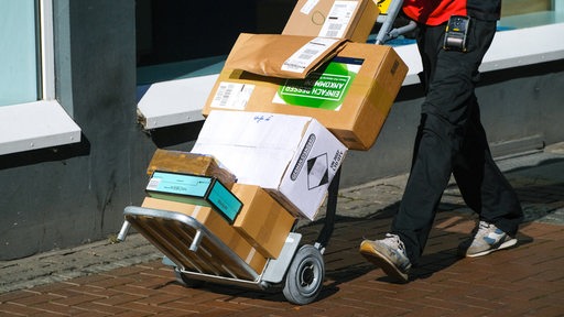 Ein Paketbote transportiert Pakete auf einer Sackkarre.