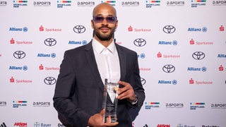 Leon Schäfer im Anzug und mit Sonnenbrille mit dem gläsernen Pokal in der Hand bei der Preisverleihung zum Para-Sportler des Jahres.