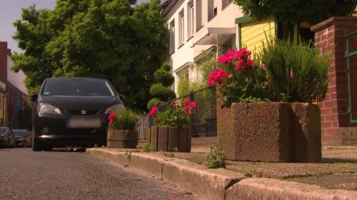 Ein Auto steht mit dem Vorderrad und dem Hinterrad auf dem Bürgersteig in einem Wohngebiet.