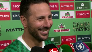 Claudio Pizarro strahlt beim Interview vor einer Werbetafel.