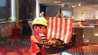 Bunte Playmobilfiguren stehen in einer Vitrine.