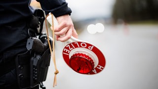 Eine Kelle in der Hand eines Polizisten, der an einer Straße steht.