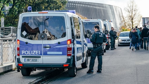 Einige Polizeiautos stehen in Reihe, ein Polizist steht daneben