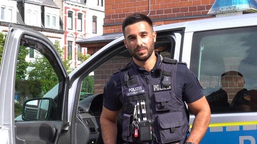 Ein Polizist steht vor einem Polizeiauto.