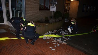 Polizisten aus Stade sammeln nach der Sprengung eines Geldautomaten vor der Filiale liegendes Bargeld ein.