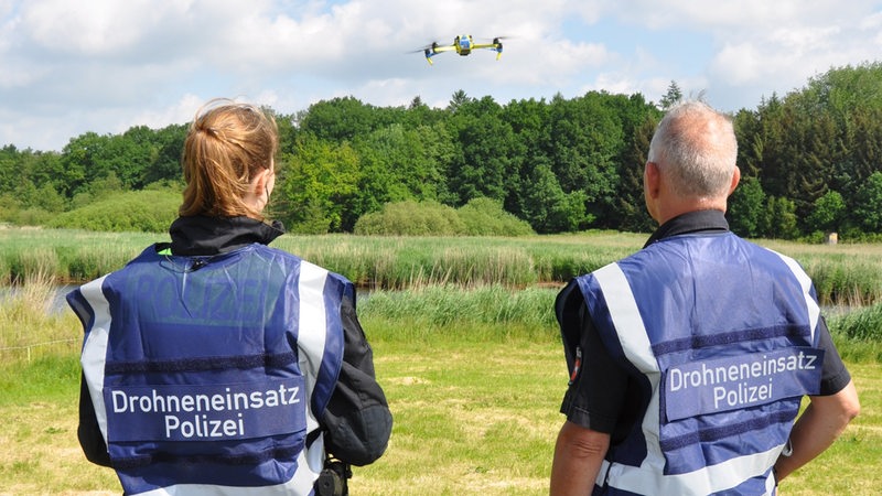 Eine Polizistin und ein Polizist lassen eine Drohne über ein Feld fliegen.