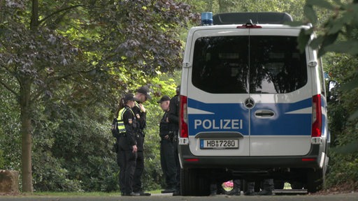 Mehrere Polizisten stehen an einem Streifenwagen an einem Friedhof