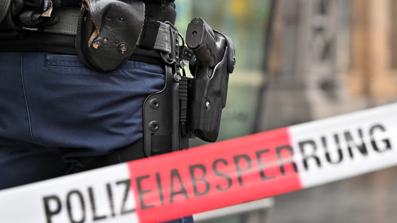 Die Waffe eines Bundespolizisten ist in seinem Holster zu sehen, davor Absperrband