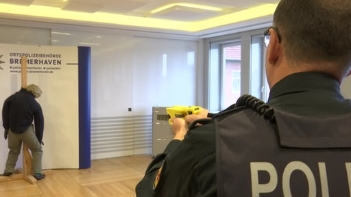 Ein Polizist zielt mit einem Taser-Gerät auf eine Dummy-Puppe.