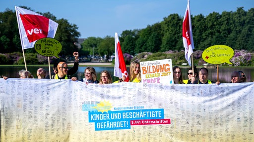 Kita-Beschäftigte stehen mit Fahnen und Plakaten vor dem Parkhotel