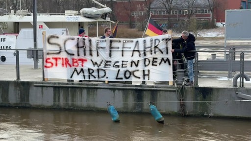 Binnenschiffer demonstrieren mit einem Protestplakat auf einem Pier.