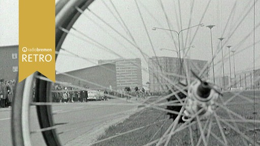 Blick durch die Speichen eines Fahrrads auf eine Straße und Hochhäuser