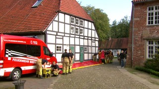 Es ist ein Feuerwehrauto und Feuerwehrmänner auf einem Bauernhof zu sehen, welche den Einsatz bei Katastrophen üben.